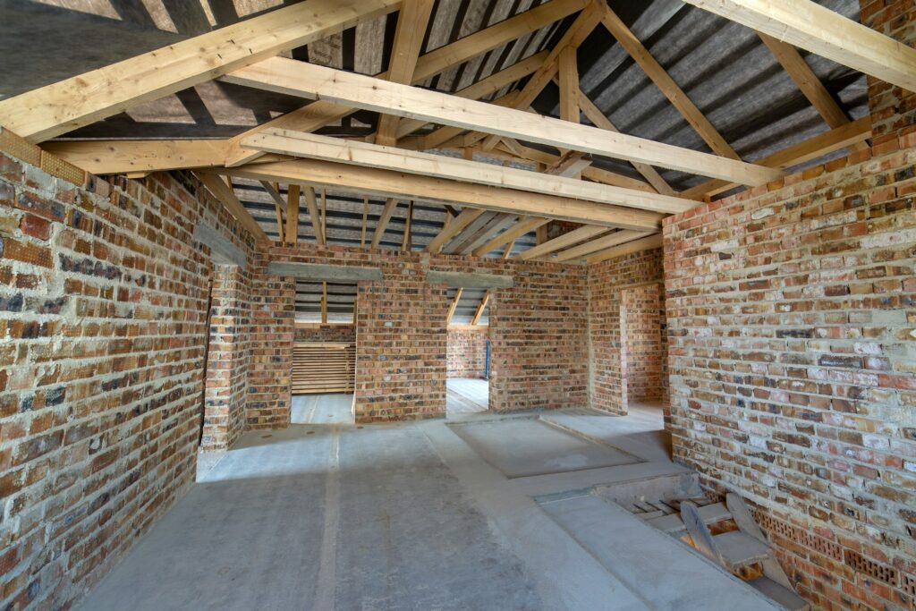 Attic of a building under construction with wooden beams of a roof structure and brick walls.