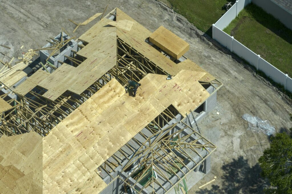 Builders working on roof construction of unfinished residential house with wooden frame