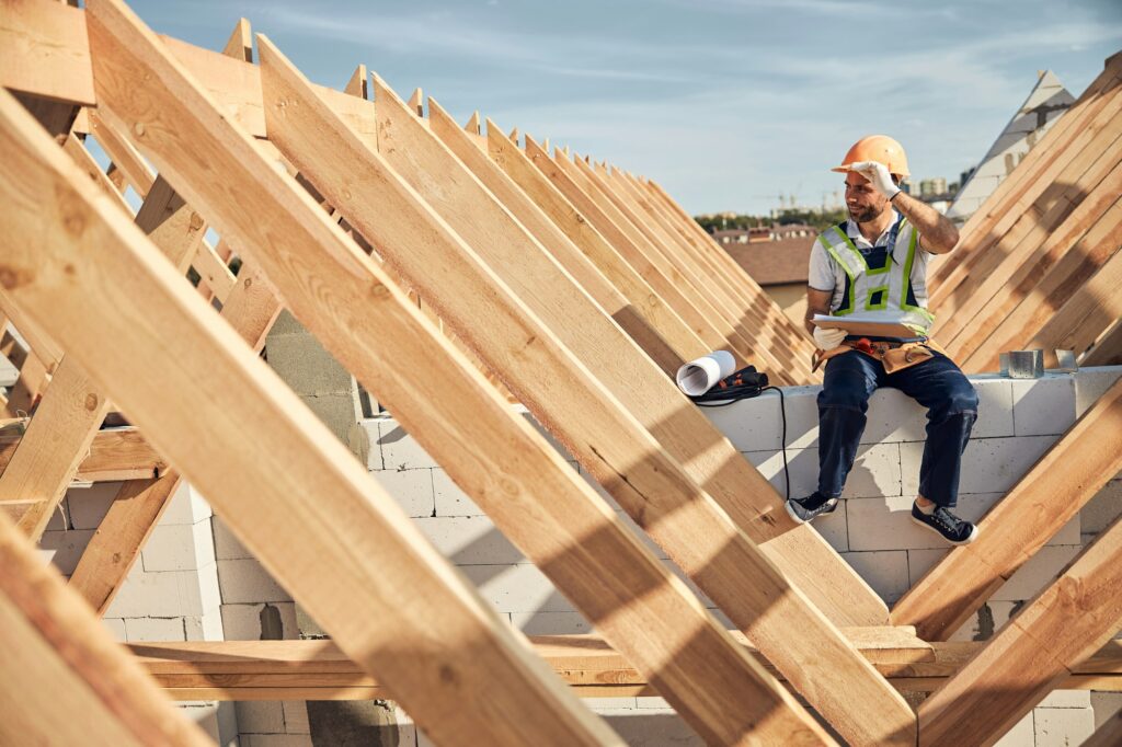 Hard-working builder sitting near a wooden roof frame