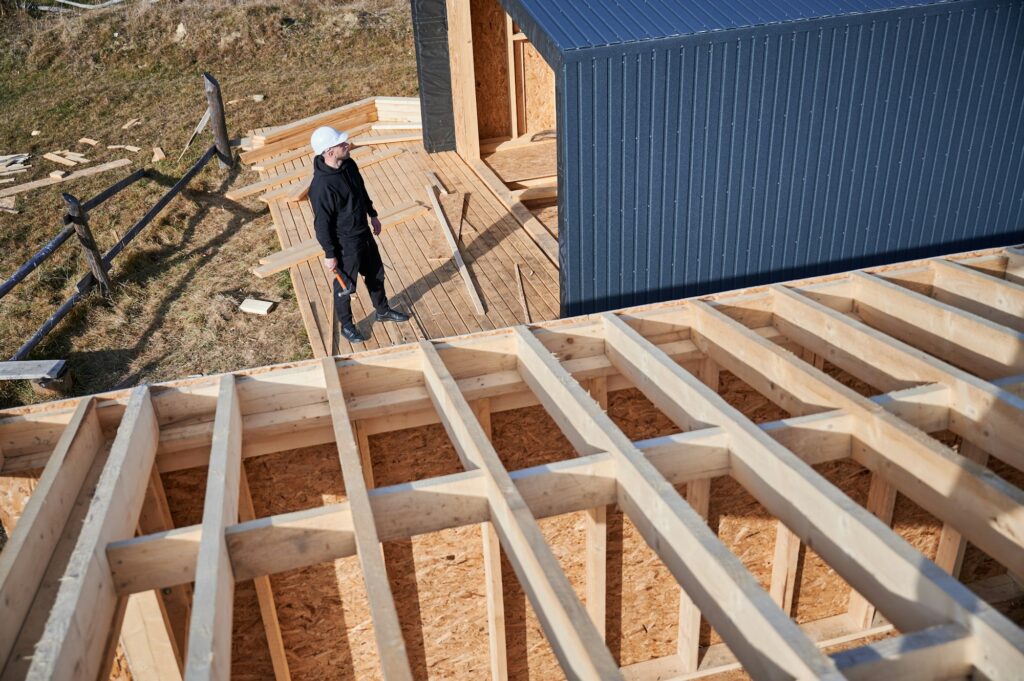 Man worker hammering while building wooden frame house.